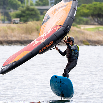 A man jumping his wingfoil on shoreline lake.