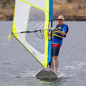 A man windsurfing with his hand extended out on shoreline lake.