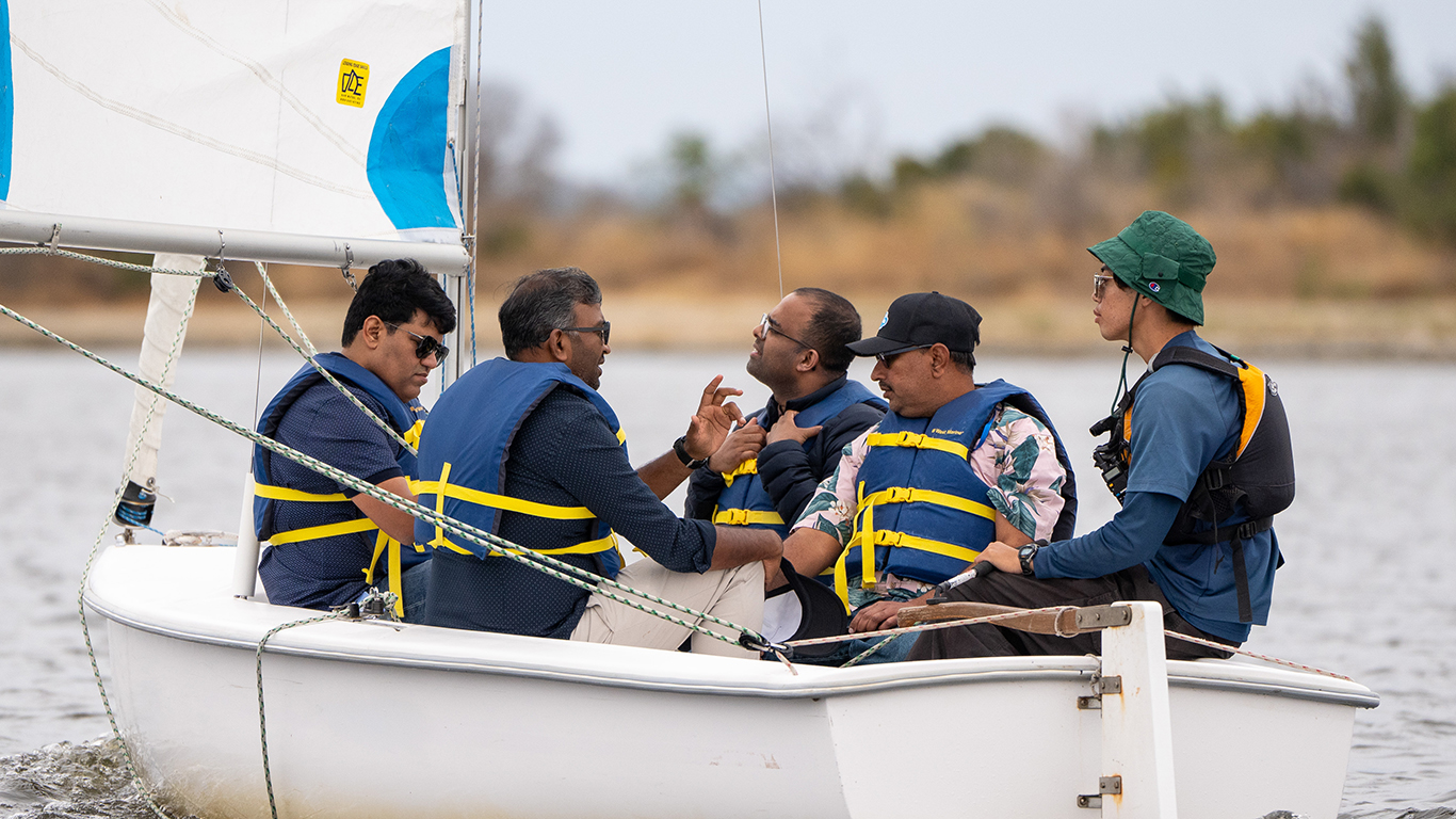 A group of men in a sailing boat having a private lesson on shoreline lake.