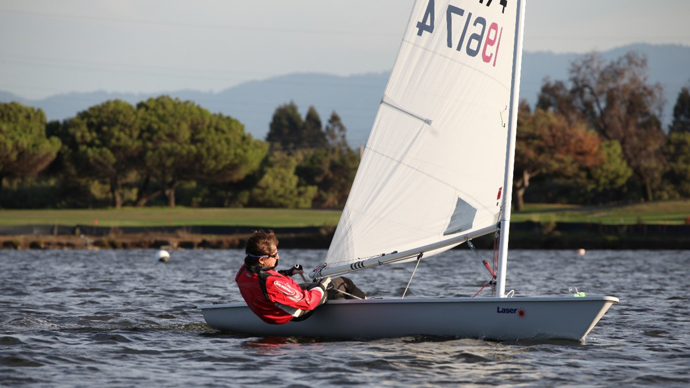 A man in a fast moving sail boat maneuvering it.