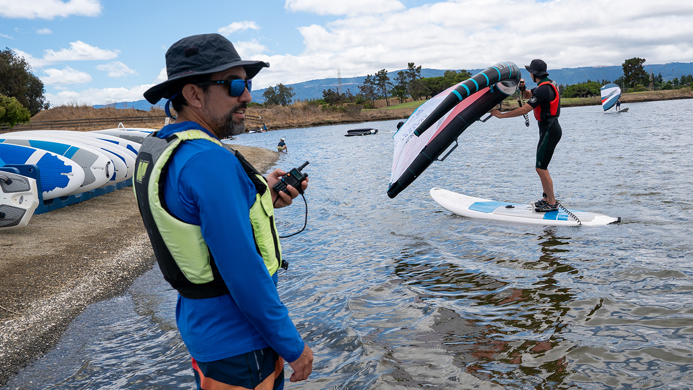 A man that works at shoreline lake holding a walkie talkie while standing in the lake.
