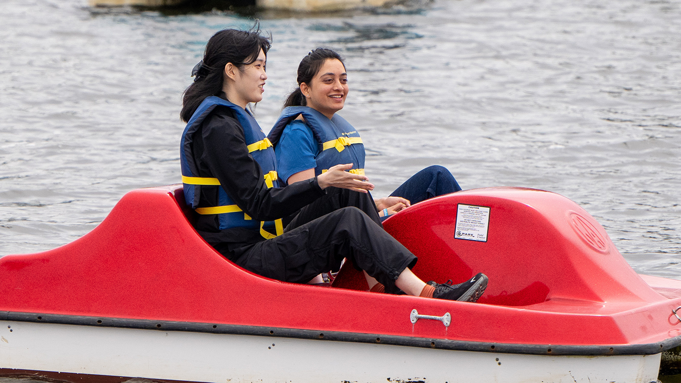 Two youn ladies in a red paddleboat on shoreline lake.