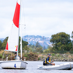  A young boy in a sail boat pulling on some of the ropes as he sails at shoreline Lake.