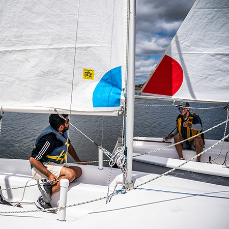 A sailing instructor teaching an adult student while their boats are docked.