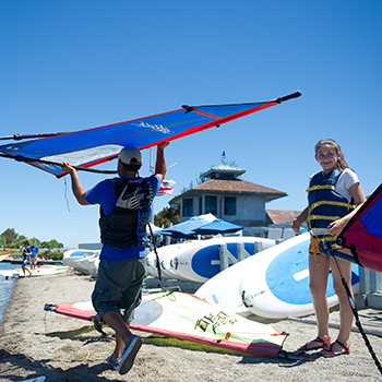 A girk on the beach getting ready to windsurf