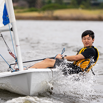 A young man in a sailboat with waves splashing.